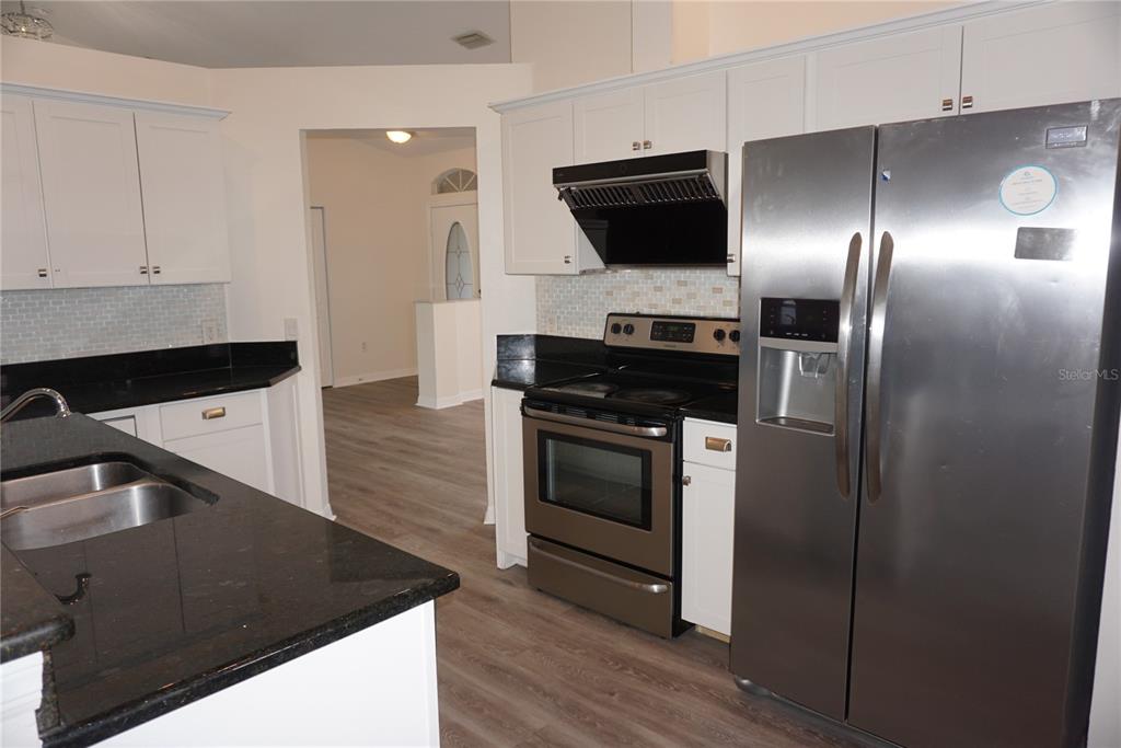 A kitchen features white cabinets, black countertops, stainless steel appliances, and light wood-look flooring — 6708 66TH AVENUE E, BRADENTON, FL