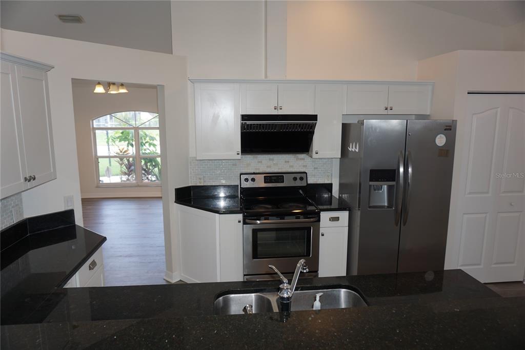 A kitchen features white cabinets, black countertops, stainless steel appliances, and a double sink — 6708 66TH AVENUE E, BRADENTON, FL