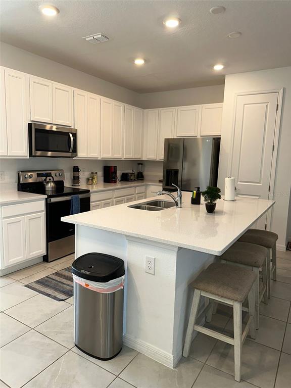 A kitchen features white cabinets, stainless steel appliances, a central island with seating, and tile flooring — 1457 DISCOVERY STREET, DAVENPORT, FL