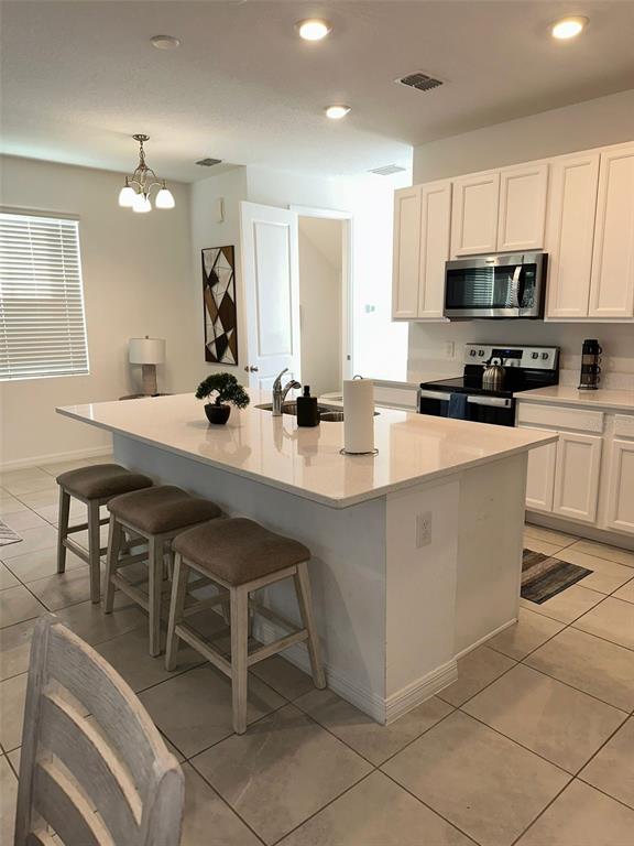 A kitchen features a white quartz island with three stools and white cabinetry — 1457 DISCOVERY STREET, DAVENPORT, FL