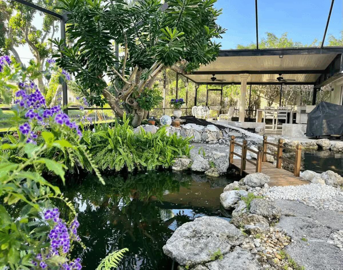 A backyard koi pond with a wooden bridge sits beneath a screened-in patio enclosure — 9823 Sun Pointe Drive, Boynton Beach FL 33437, BOYNTON BEACH, FL
