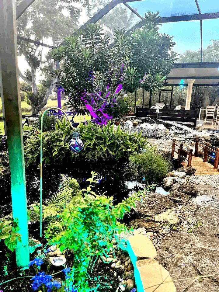 A screened-in patio features a koi pond, a small wooden bridge, and lush landscaping — 9823 Sun Pointe Drive, Boynton Beach FL 33437, BOYNTON BEACH, FL