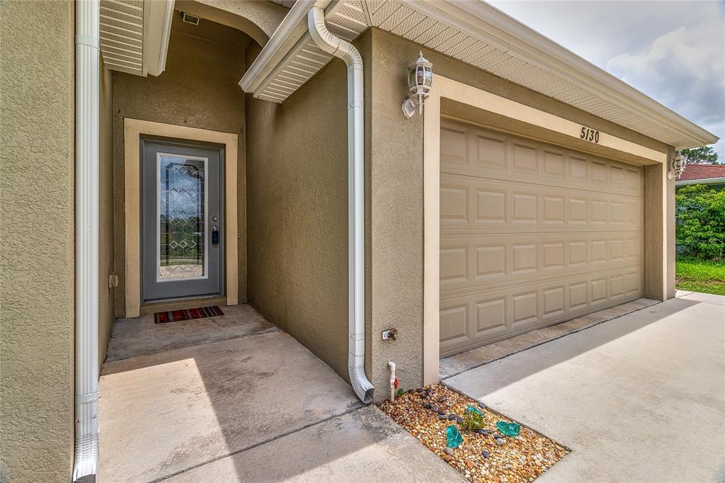 A beige house exterior features a gray front door and a tan garage door — 5130 20TH STREET, ZEPHYRHILLS, FL