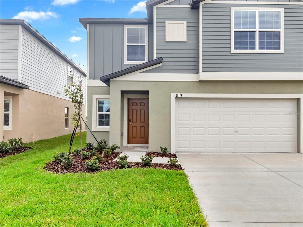 A two-story house exterior features a brown front door, a garage, and gray siding — 13118 EMPRESS JEWEL TRAIL, PARRISH, FL