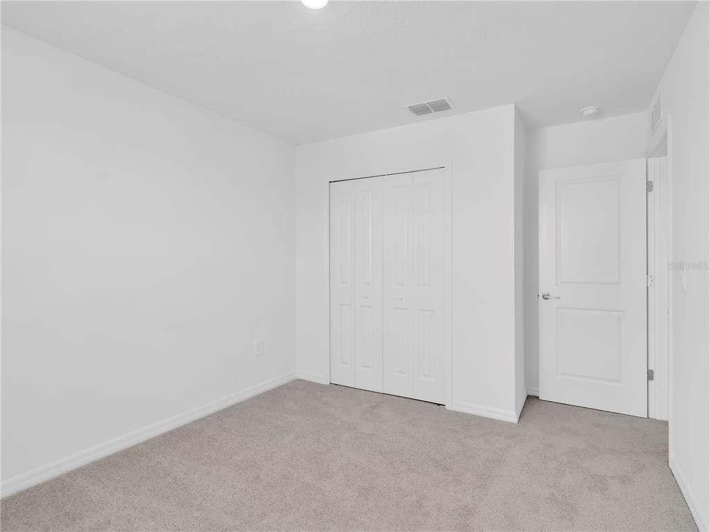 An empty bedroom features white walls, gray carpeting, a bi-fold closet, and a white door — 13118 EMPRESS JEWEL TRAIL, PARRISH, FL