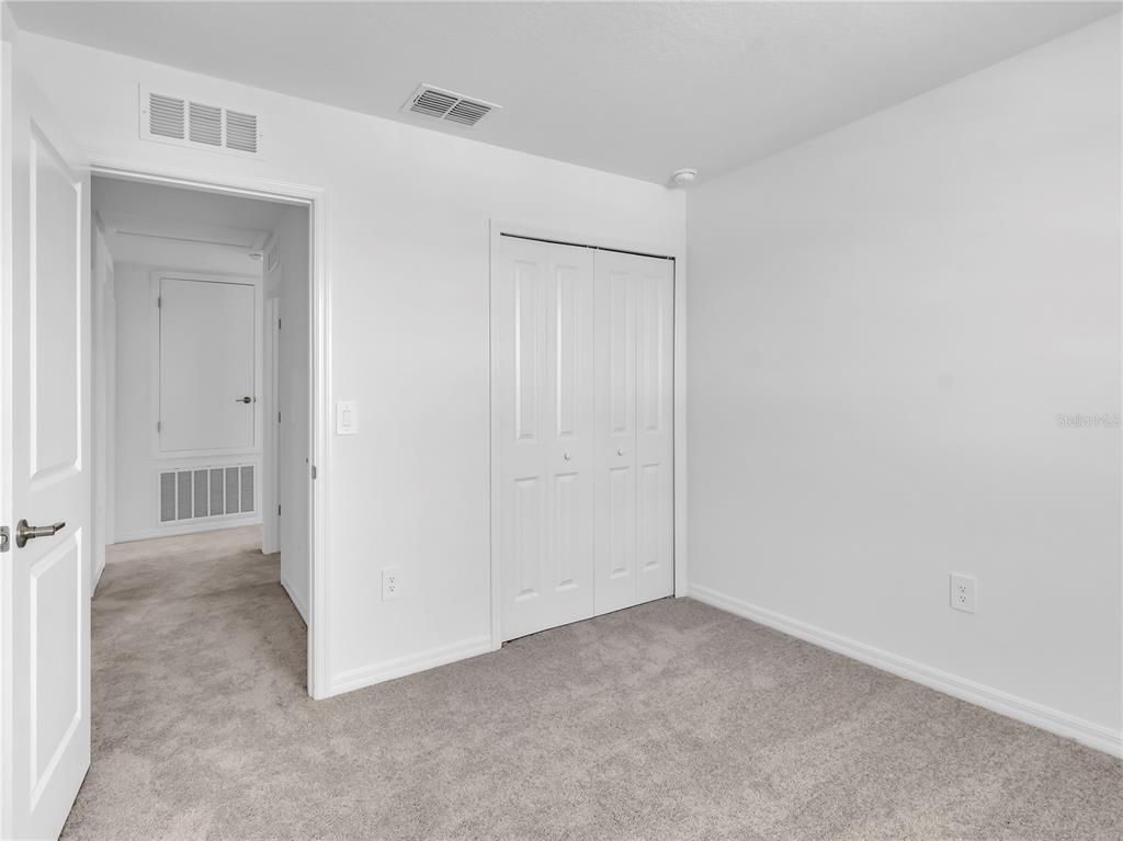 An empty bedroom features white walls, gray carpeting, and a white bi-fold closet door — 13118 EMPRESS JEWEL TRAIL, PARRISH, FL