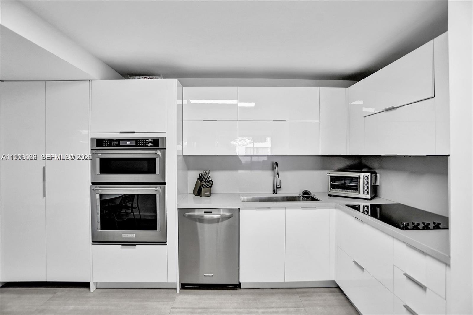 A modern kitchen features white glossy cabinets, stainless steel appliances, and light-colored countertops — 2500 Parkview Dr # 1912, Hallandale Beach FL 33009, HALLANDALE BEACH, FL