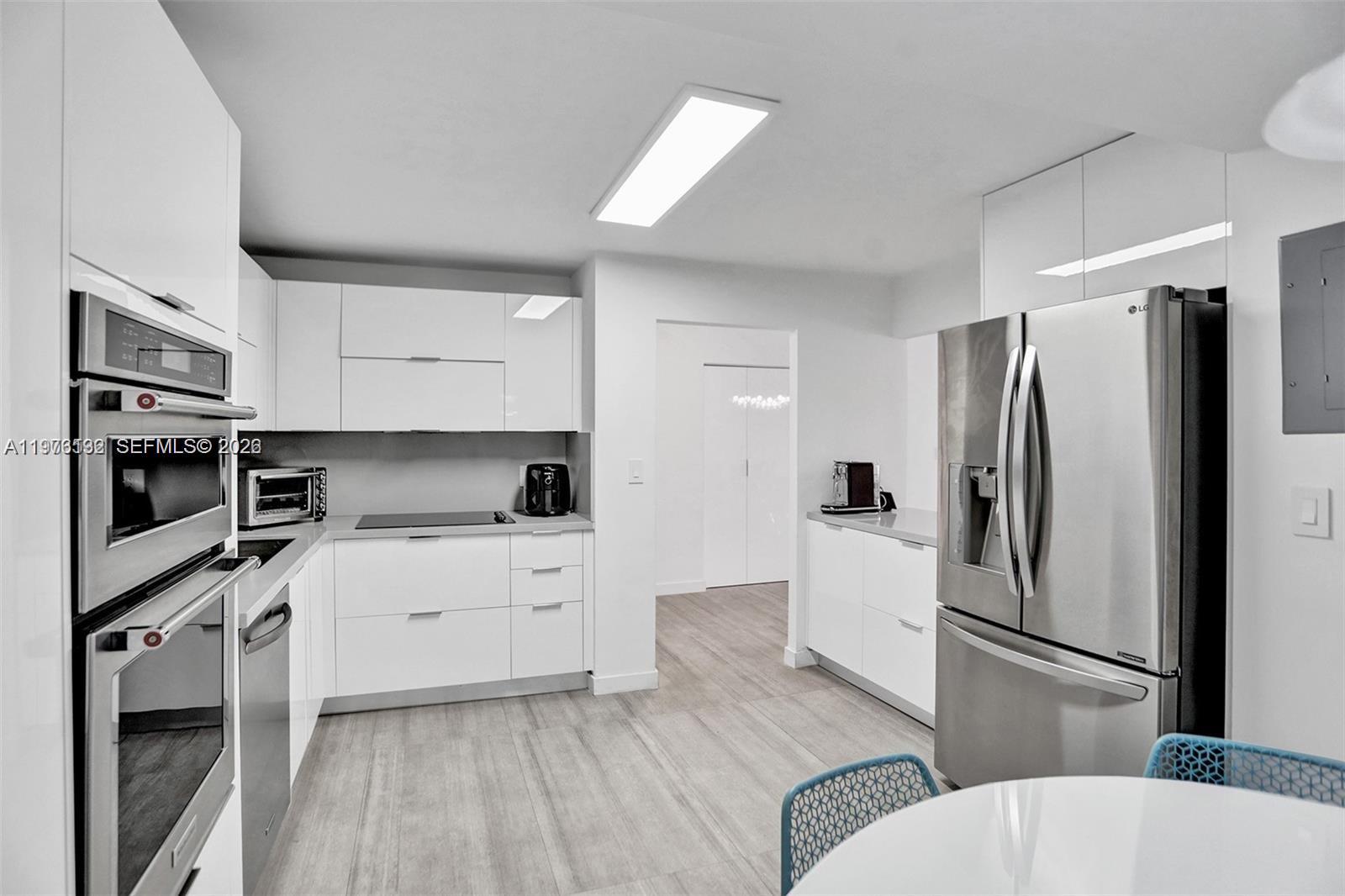 A modern kitchen features white cabinetry, stainless steel appliances, and light wood-look flooring — 2500 Parkview Dr # 1912, Hallandale Beach FL 33009, HALLANDALE BEACH, FL