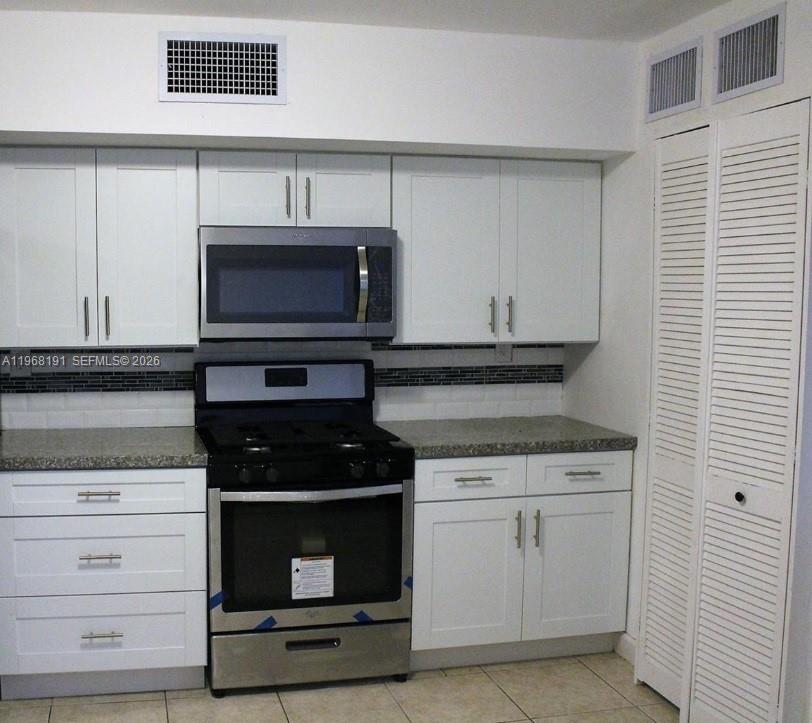 A kitchen features white cabinets, a stainless steel microwave, a gas range, and tiled flooring — 7133 SW 109th Ct, Miami FL 33173, MIAMI, FL