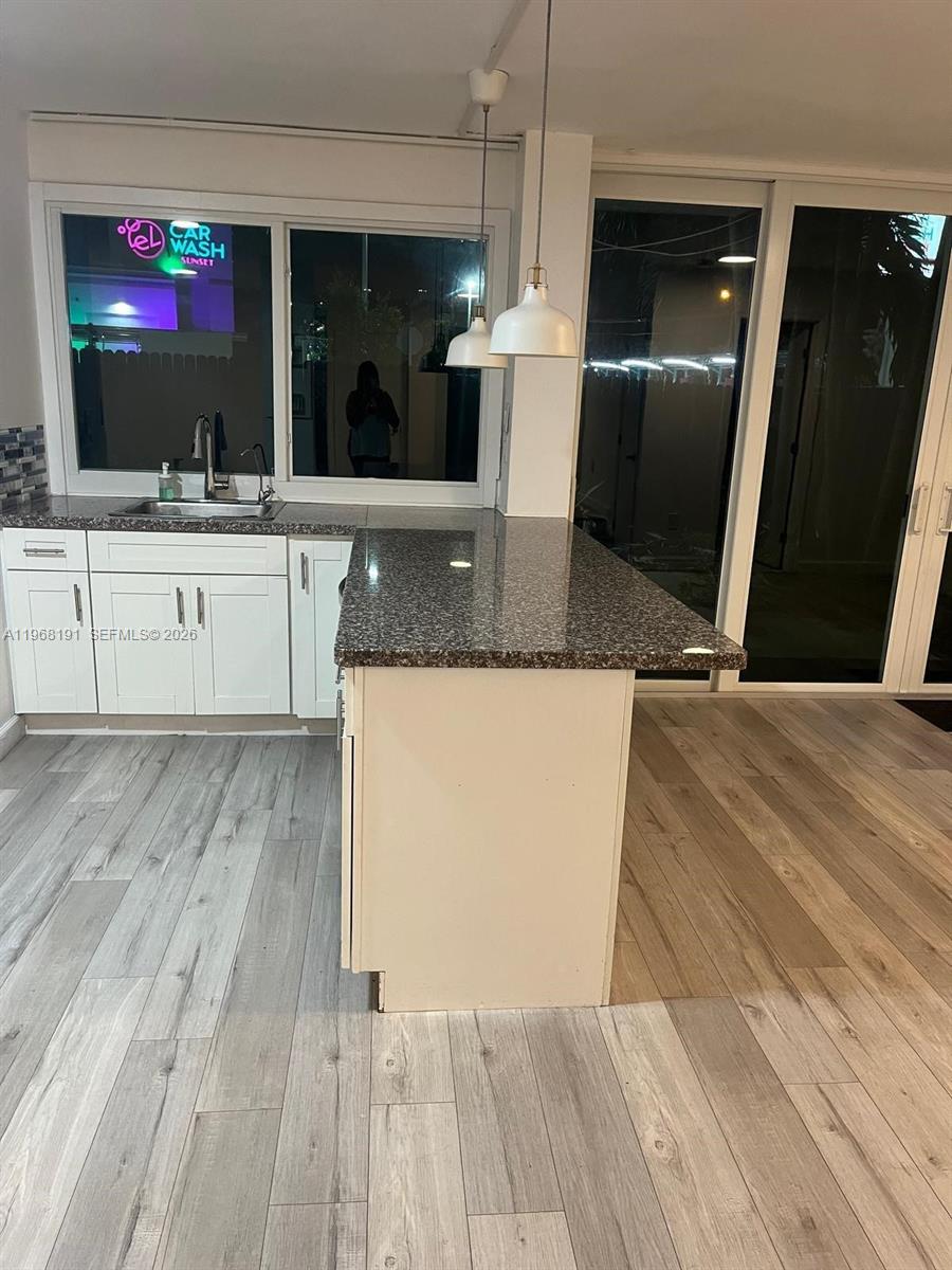 A kitchen features white cabinets, a granite countertop island, and wood-look flooring — 7133 SW 109th Ct, Miami FL 33173, MIAMI, FL