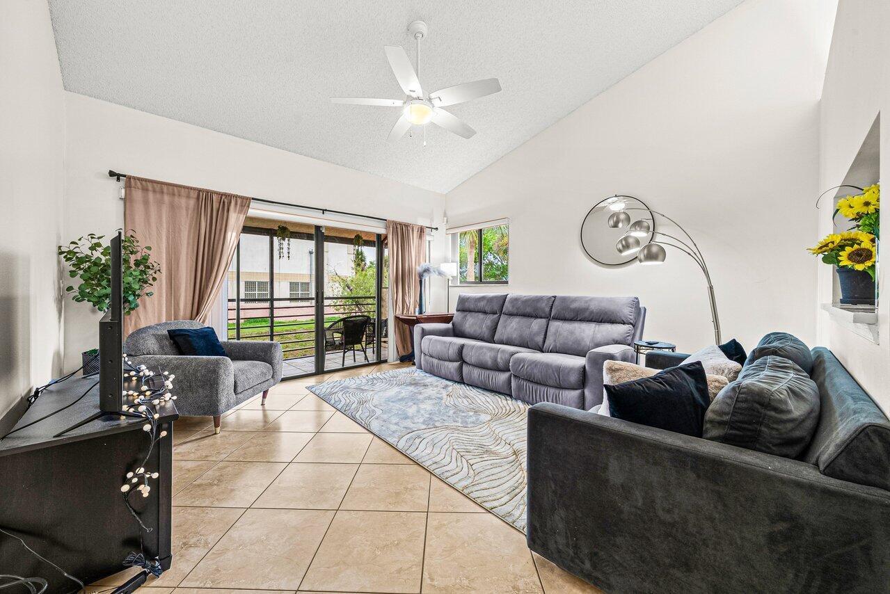 A living room features tile flooring, a vaulted ceiling, a ceiling fan, and sliding glass doors — 16 Via De Casas Sur # 204, Boynton Beach FL 33426, BOYNTON BEACH, FL
