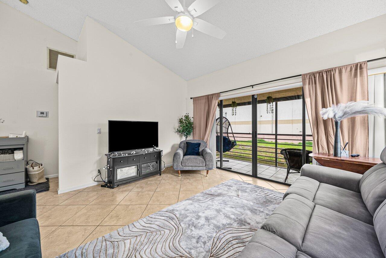 A living room features tile floors, a gray sofa, a television console, and sliding glass doors — 16 Via De Casas Sur # 204, Boynton Beach FL 33426, BOYNTON BEACH, FL