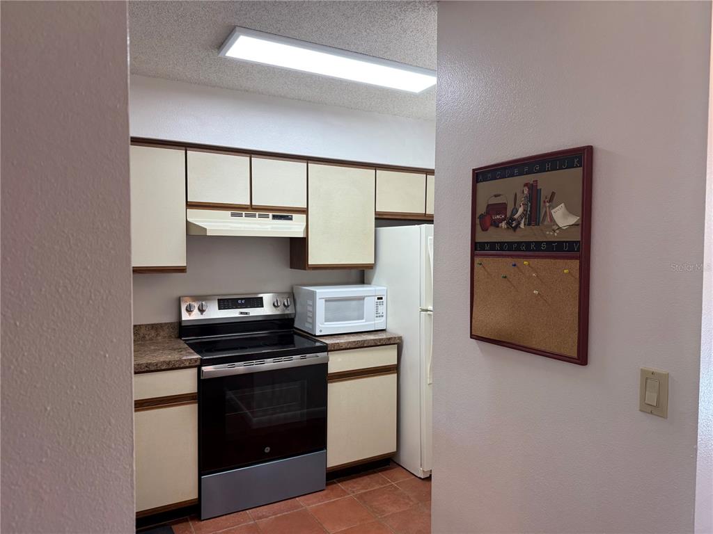 A kitchen features off-white cabinets, a black stove, a white microwave, and a corkboard — 6519 SPRING FLOWER DRIVE UNIT 22, NEW PORT RICHEY, FL