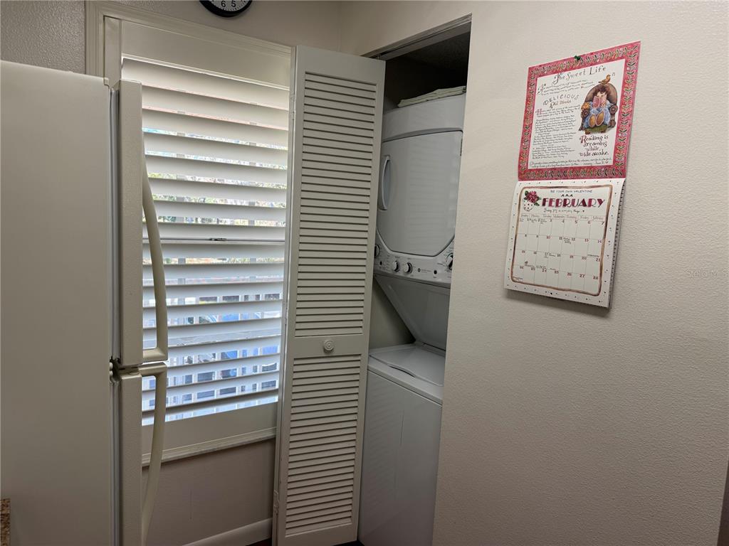 A laundry closet with a stacked washer and dryer sits next to a window with shutters — 6519 SPRING FLOWER DRIVE UNIT 22, NEW PORT RICHEY, FL