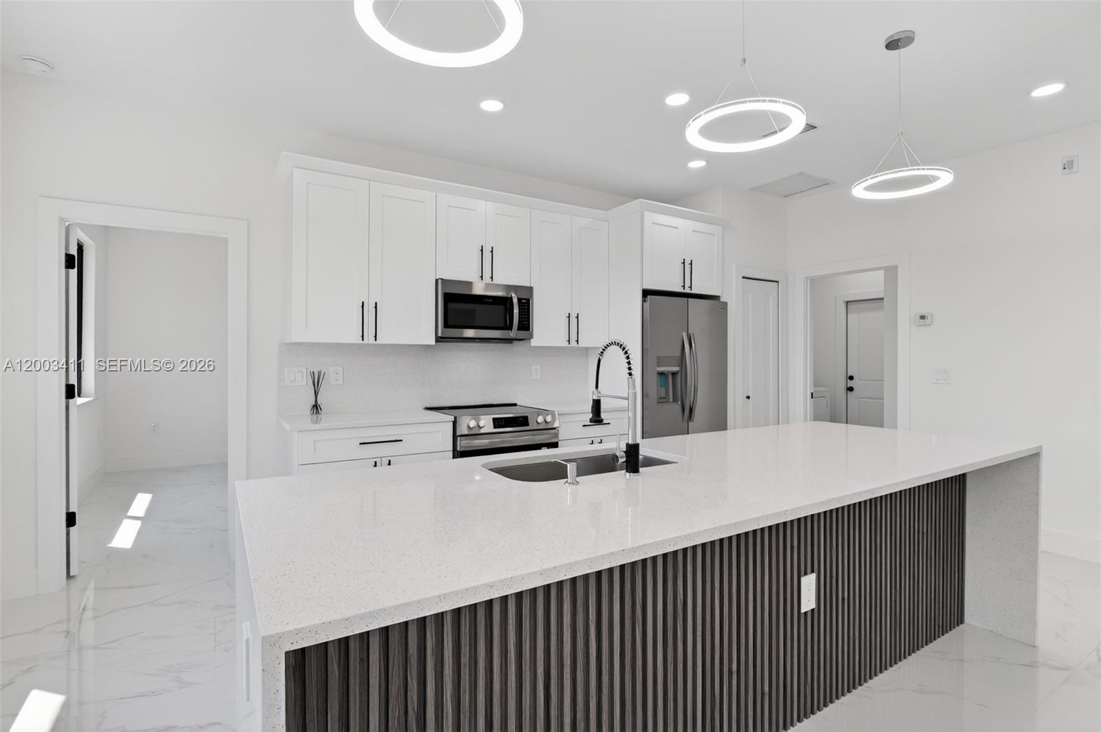 A modern kitchen features white cabinetry, stainless steel appliances, and a slatted wood kitchen island — 312 Rand Ave., Lehigh Acres FL 33974, LEHIGH ACRES, FL