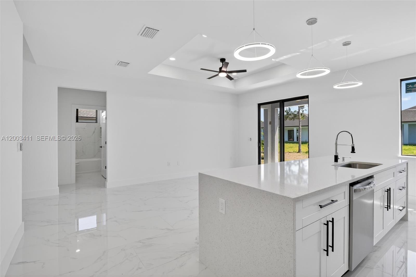 A modern kitchen with a white quartz island and marble floors opens to a living area — 312 Rand Ave., Lehigh Acres FL 33974, LEHIGH ACRES, FL