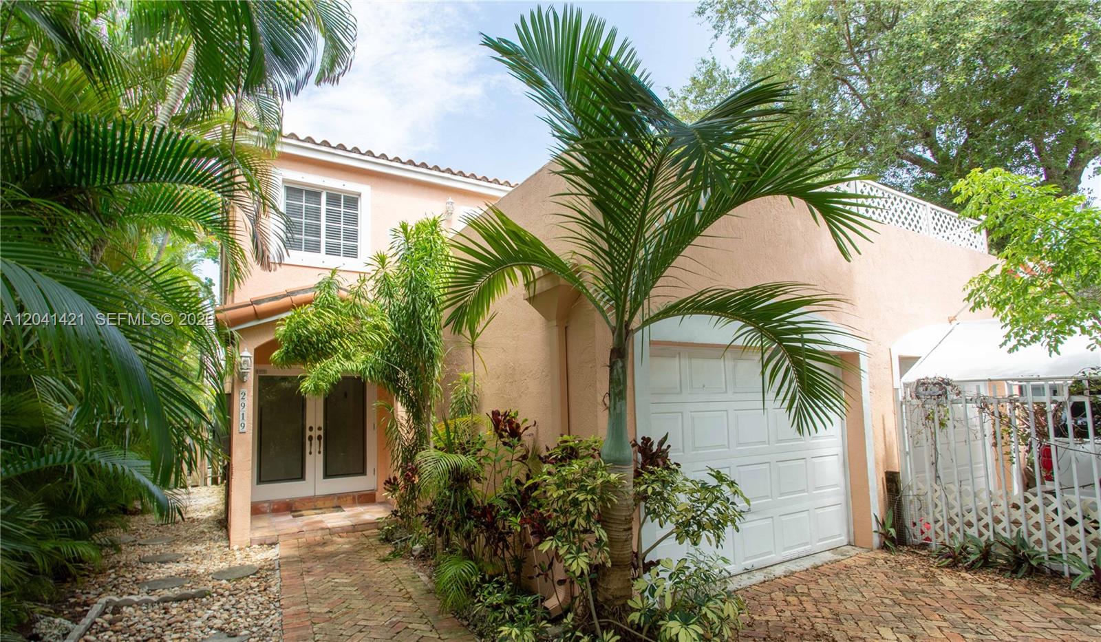 A two-story peach-colored house features a white garage door, palm trees, and brick walkway — 2919 Virginia St, Miami FL 33133, MIAMI, FL