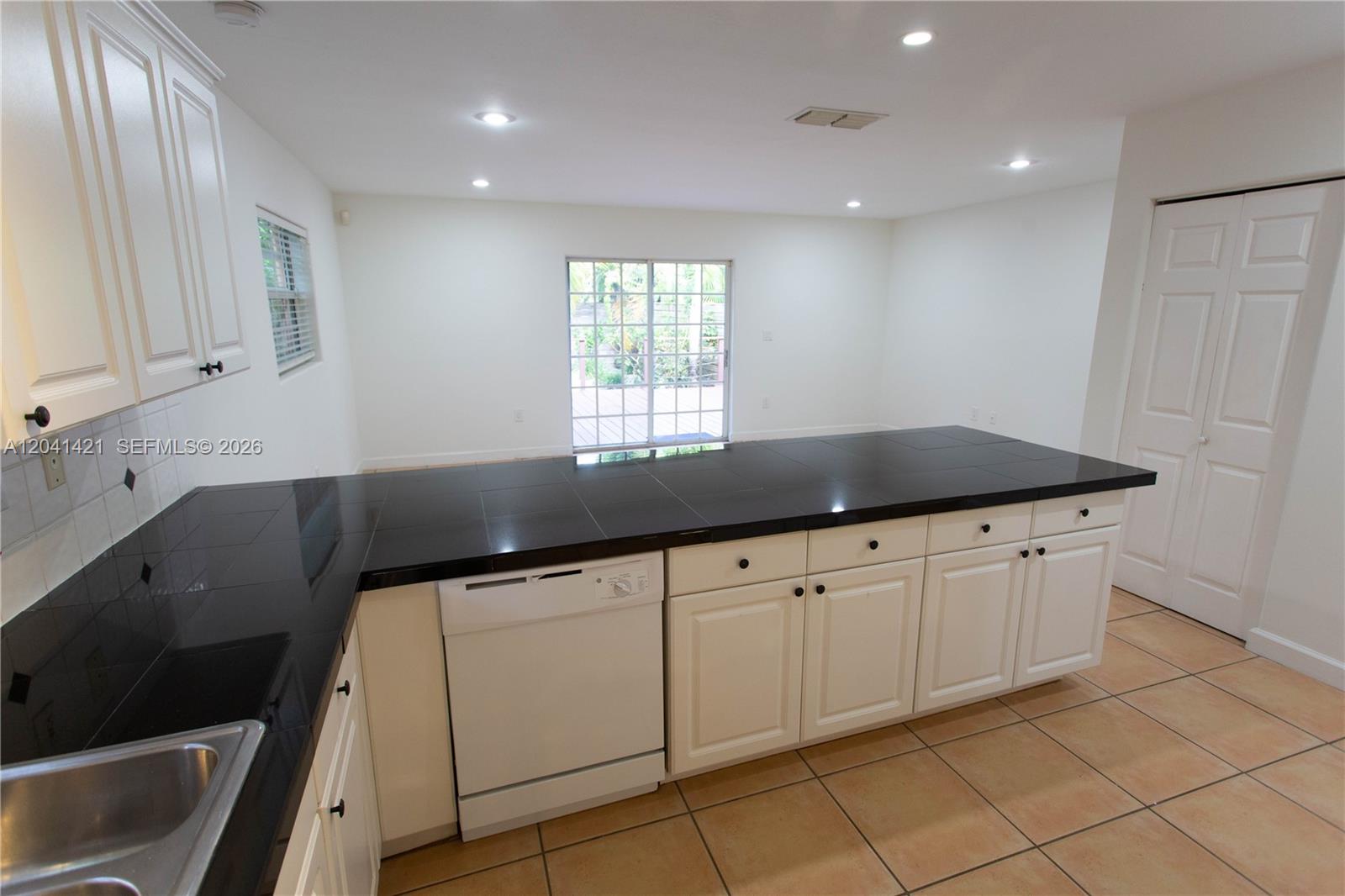 A kitchen features white cabinets, black tiled countertops, a white dishwasher, and beige floor tiles — 2919 Virginia St, Miami FL 33133, MIAMI, FL