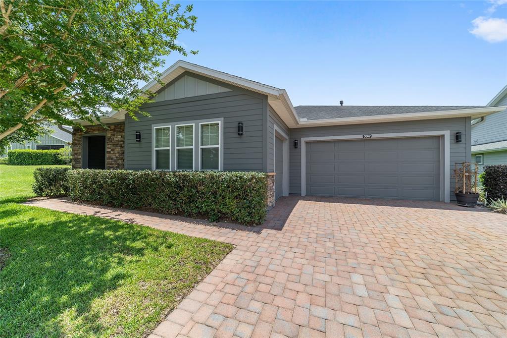 A gray house with a stone accent wall, a paved driveway, and a manicured hedge — 3862 NW 49TH COURT, OCALA, FL