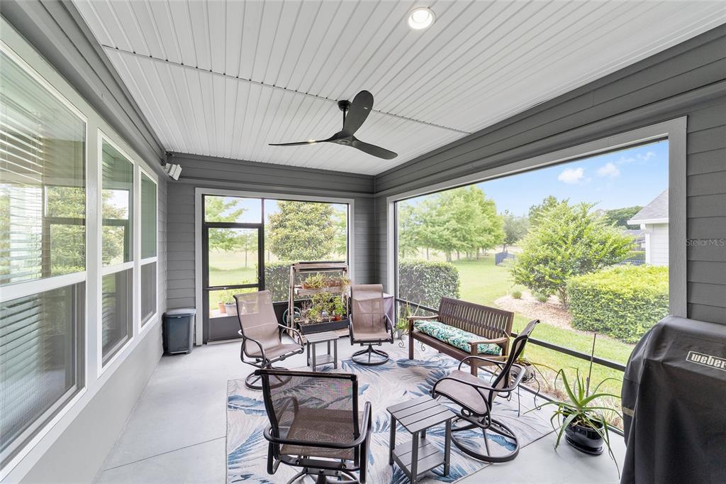 A screened-in porch features gray siding, a ceiling fan, and outdoor furniture on a rug — 3862 NW 49TH COURT, OCALA, FL