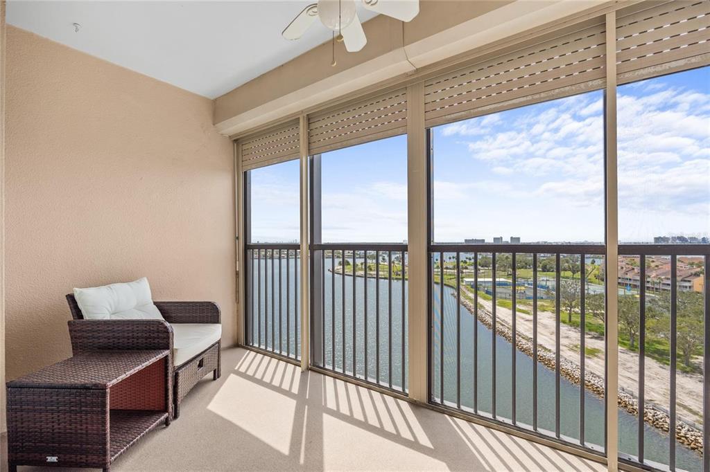 A balcony with wicker furniture, a ceiling fan, and a view of a waterway — 10355 PARADISE BOULEVARD UNIT 907, TREASURE ISLAND, FL
