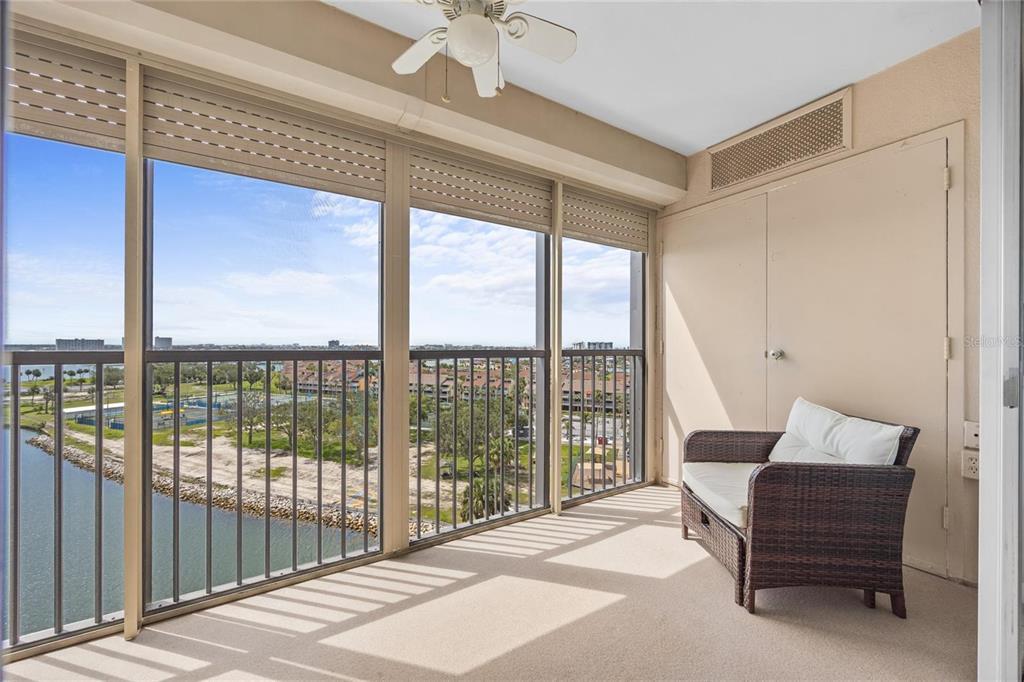 A sunroom with a wicker chair, ceiling fan, and floor-to-ceiling windows overlooking a waterfront view — 10355 PARADISE BOULEVARD UNIT 907, TREASURE ISLAND, FL