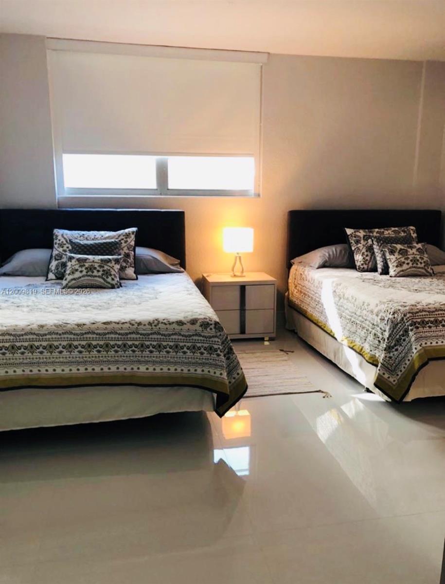A bedroom features two beds with patterned bedding, a central nightstand with a lamp, and tile flooring — 3801 S Ocean Dr # 2B, Hollywood FL 33019, HOLLYWOOD, FL