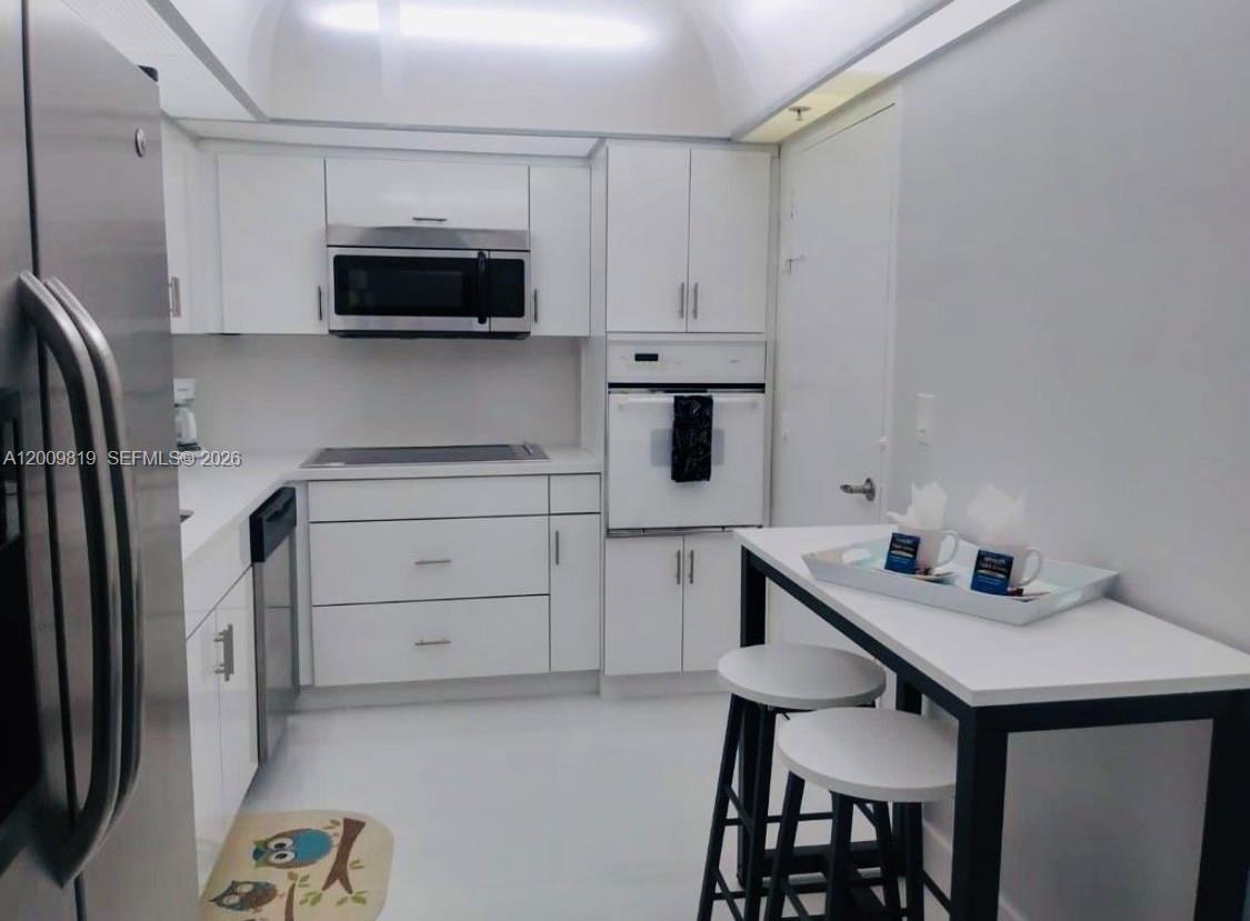 A white kitchen features stainless steel appliances, a breakfast table with stools, and white cabinetry — 3801 S Ocean Dr # 2B, Hollywood FL 33019, HOLLYWOOD, FL