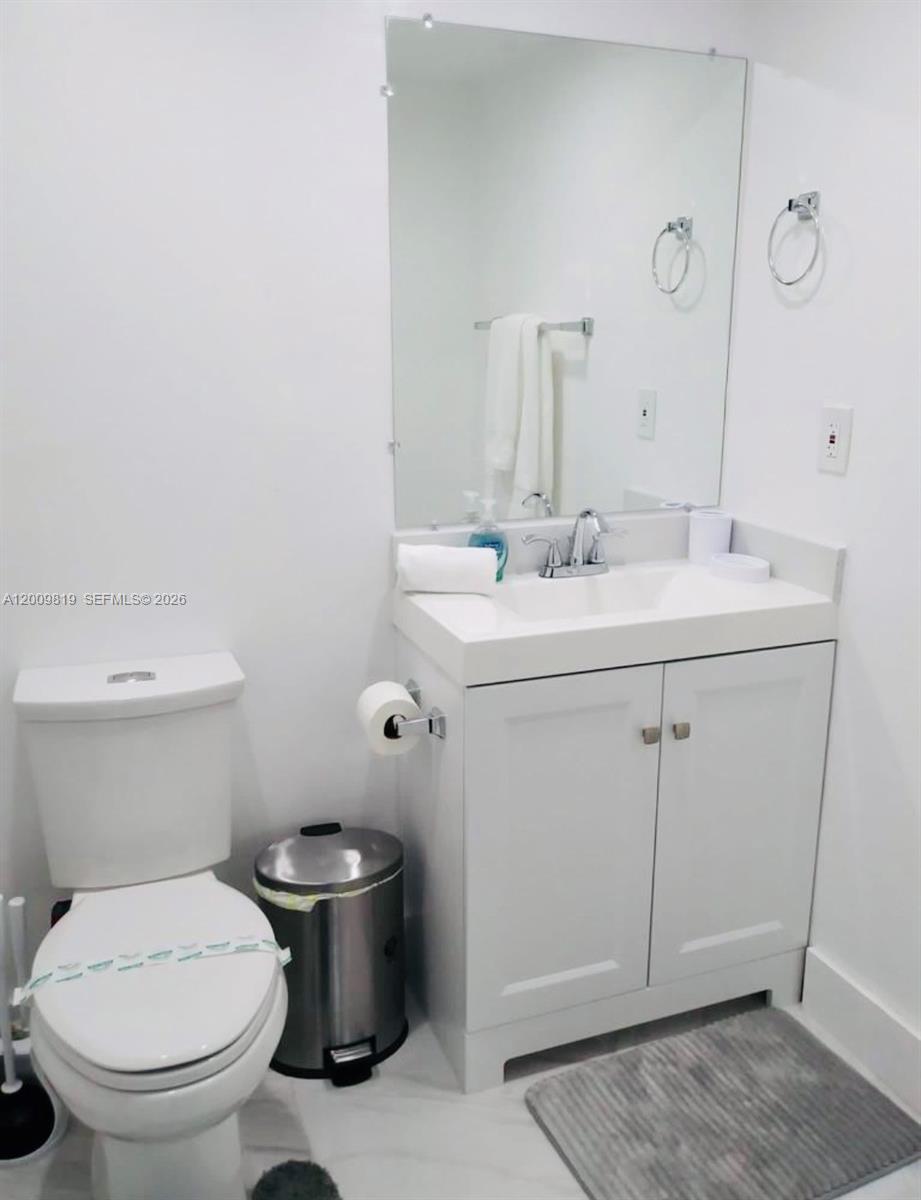 A small bathroom features a white vanity, a toilet, and a wall-mounted mirror — 3801 S Ocean Dr # 2B, Hollywood FL 33019, HOLLYWOOD, FL