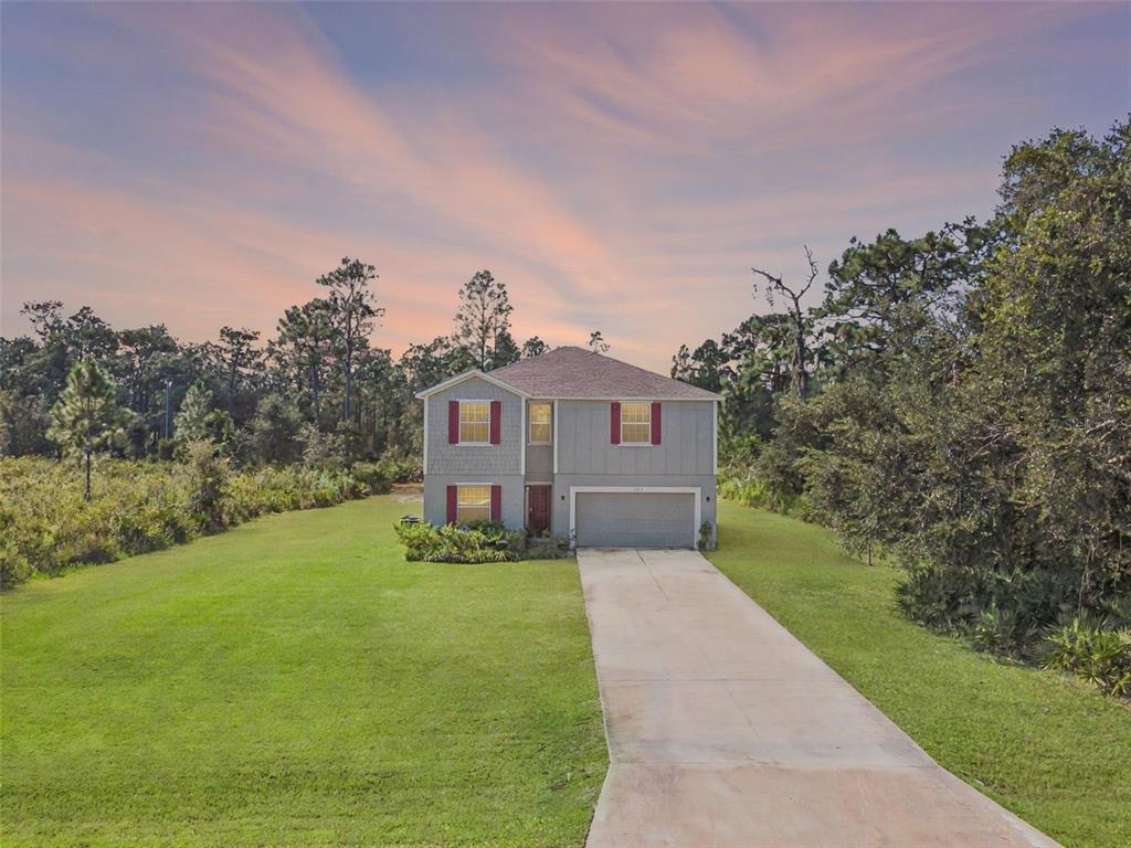 A two-story house with a gray exterior, red shutters, and a concrete driveway at sunset — 3681 MAGNOLIA DRIVE, INDIAN LAKE ESTATES, FL