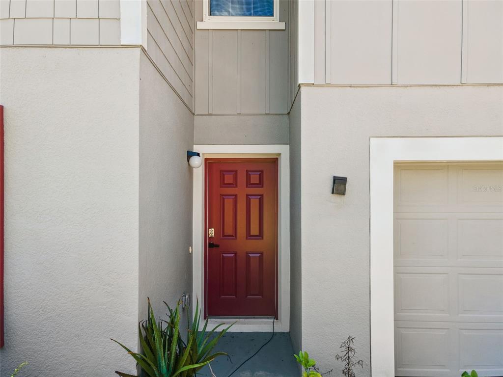 A red front door is recessed between a gray exterior wall and a garage door — 3681 MAGNOLIA DRIVE, INDIAN LAKE ESTATES, FL