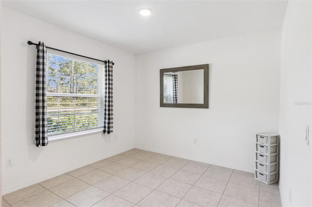 A bright room with white walls, tiled flooring, a window with checkered curtains, and a mirror — 3681 MAGNOLIA DRIVE, INDIAN LAKE ESTATES, FL