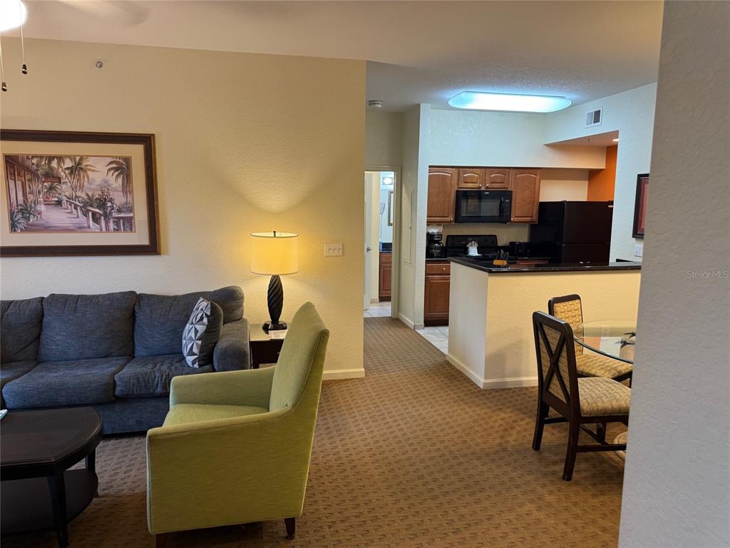 A living room with a gray sofa and green armchair opens to a kitchen area — 8112 POINCIANA BOULEVARD UNIT 1206, ORLANDO, FL