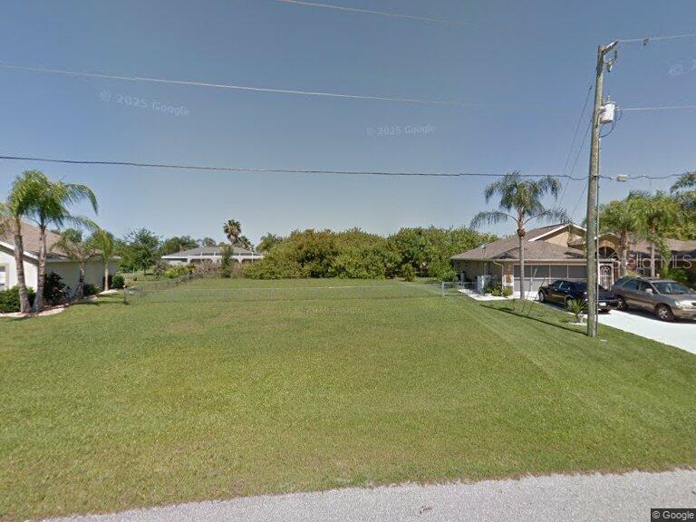 A vacant, grassy residential lot sits between two houses under a clear blue sky — 177 CASTILE COURT, PUNTA GORDA, FL