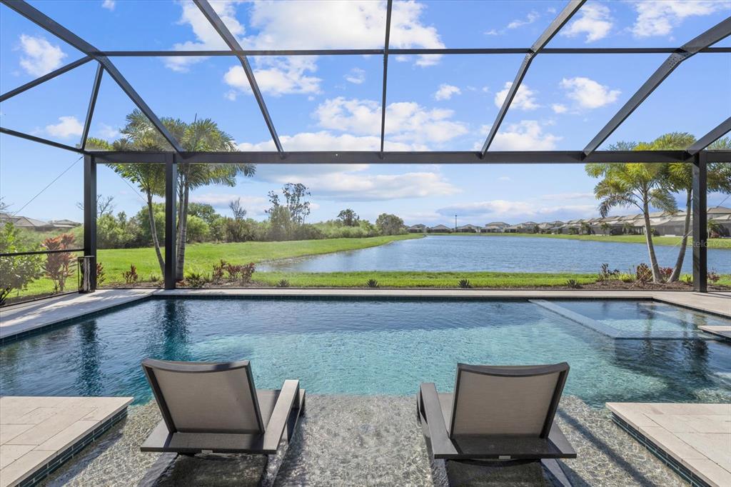 A screened-in pool patio features two lounge chairs on a tanning ledge overlooking a lake — 4618 SWEET RETREAT RUN, LAKEWOOD RANCH, FL