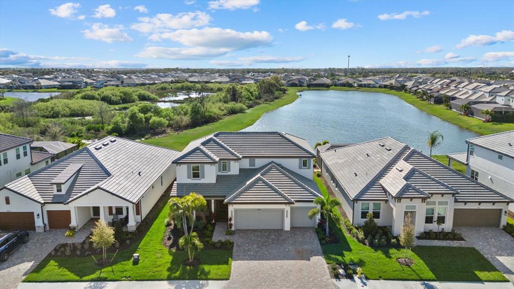 An aerial view shows three suburban houses with tiled roofs situated next to a pond — 4618 SWEET RETREAT RUN, LAKEWOOD RANCH, FL