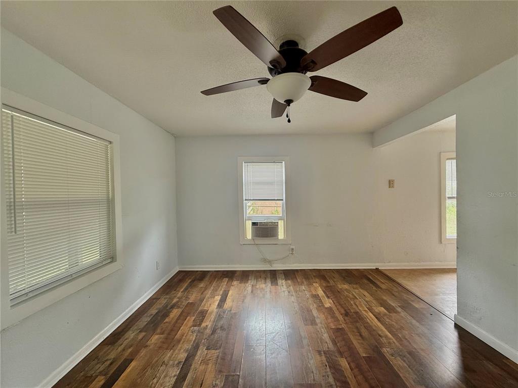An empty room features wood-look flooring, a ceiling fan, and a window air conditioning unit — 7581 S MYERS POINT, FLORAL CITY, FL