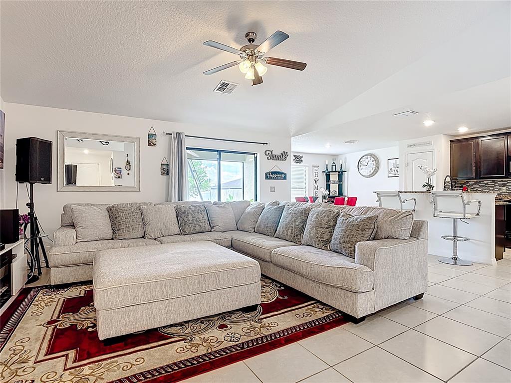 A living room features a large sectional sofa, an ottoman, and a red area rug — 26 ORCHID COURT, KISSIMMEE, FL