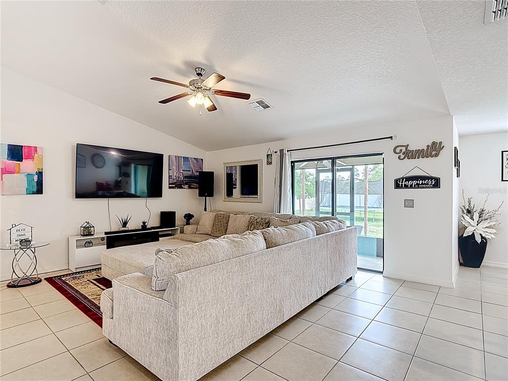 A living room features a large sectional sofa, a wall-mounted television, and tile flooring — 26 ORCHID COURT, KISSIMMEE, FL