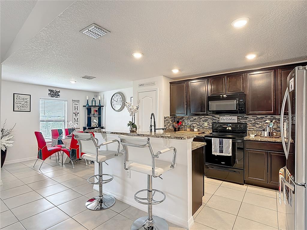 A kitchen features dark wood cabinets, granite countertops, a breakfast bar with stools, and tile flooring — 26 ORCHID COURT, KISSIMMEE, FL
