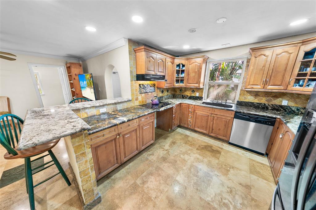 A kitchen features wood cabinets, granite countertops, a tile backsplash, and stone flooring — 332 FLETCHER AVENUE, DAYTONA BEACH, FL