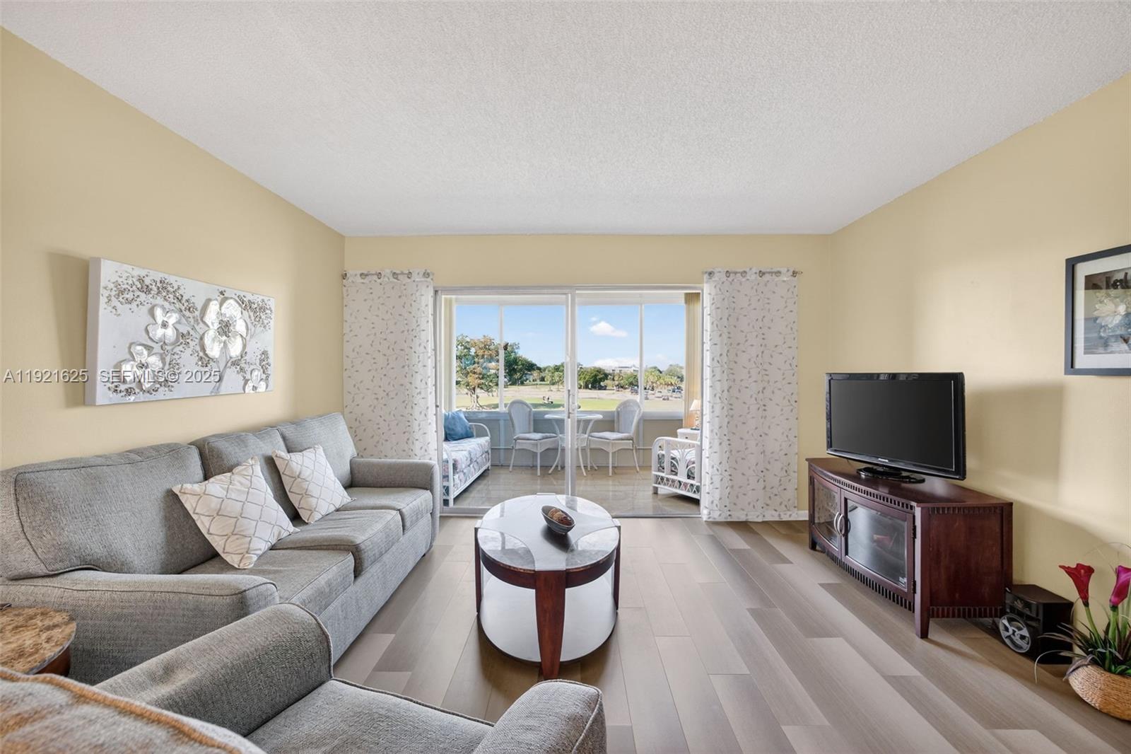 A living room features a grey sofa, coffee table, television, and sliding doors to a balcony — 7817 Golf Circle Dr # 301, Margate FL 33063, MARGATE, FL
