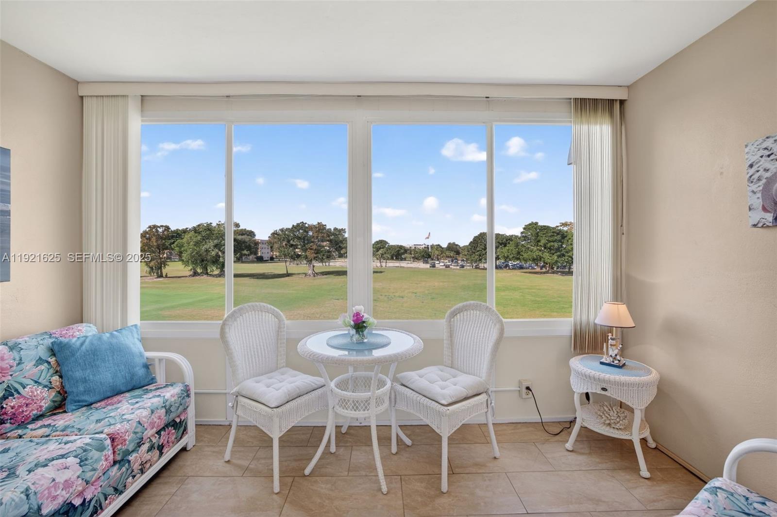 A sunroom features a floral sofa, a bistro set, and large windows overlooking a golf course — 7817 Golf Circle Dr # 301, Margate FL 33063, MARGATE, FL
