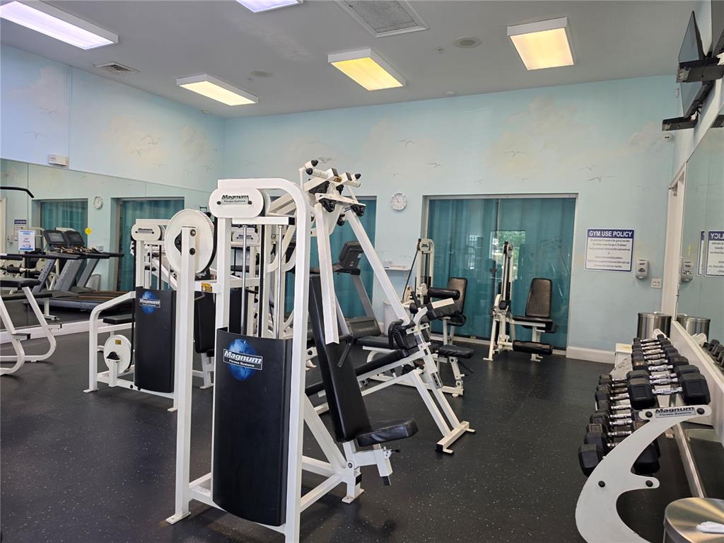 A gym room features various weight machines, a dumbbell rack, and light blue wall murals — 3016 BONFIRE BEACH DRIVE UNIT 103, KISSIMMEE, FL