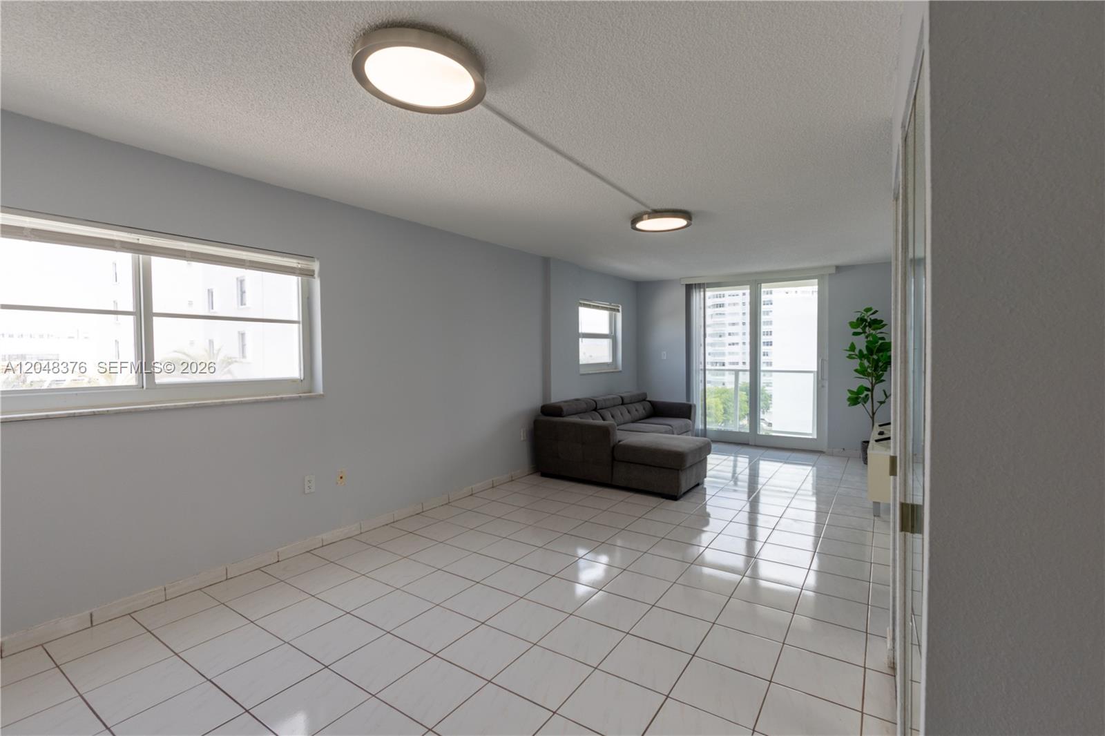 A living room with light blue walls, white tile flooring, and a grey sectional sofa — 1750 James Ave # 7L, Miami Beach FL 33139, MIAMI BEACH, FL