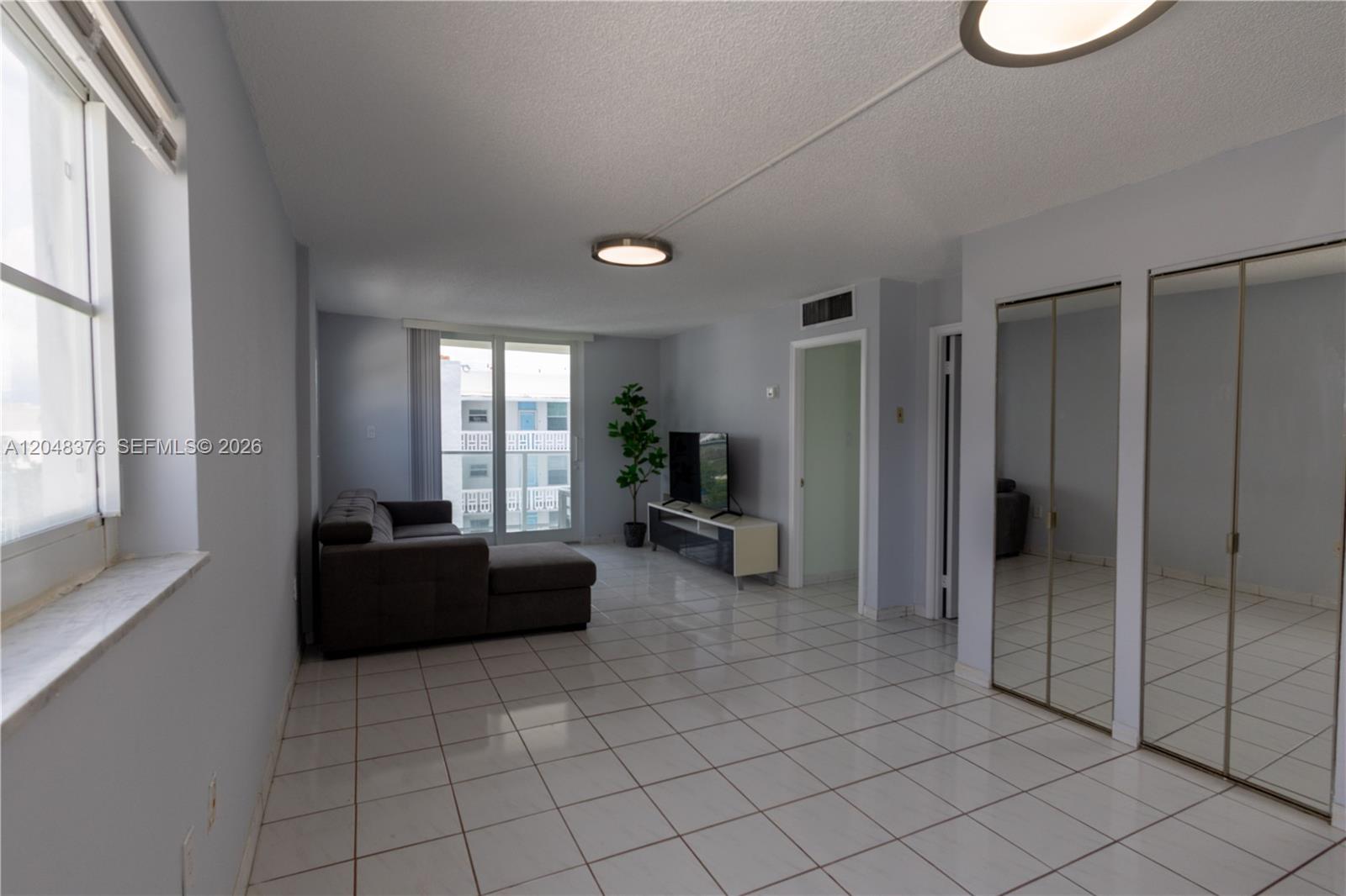 A living room features white tile floors, a grey sectional sofa, and mirrored closet doors — 1750 James Ave # 7L, Miami Beach FL 33139, MIAMI BEACH, FL