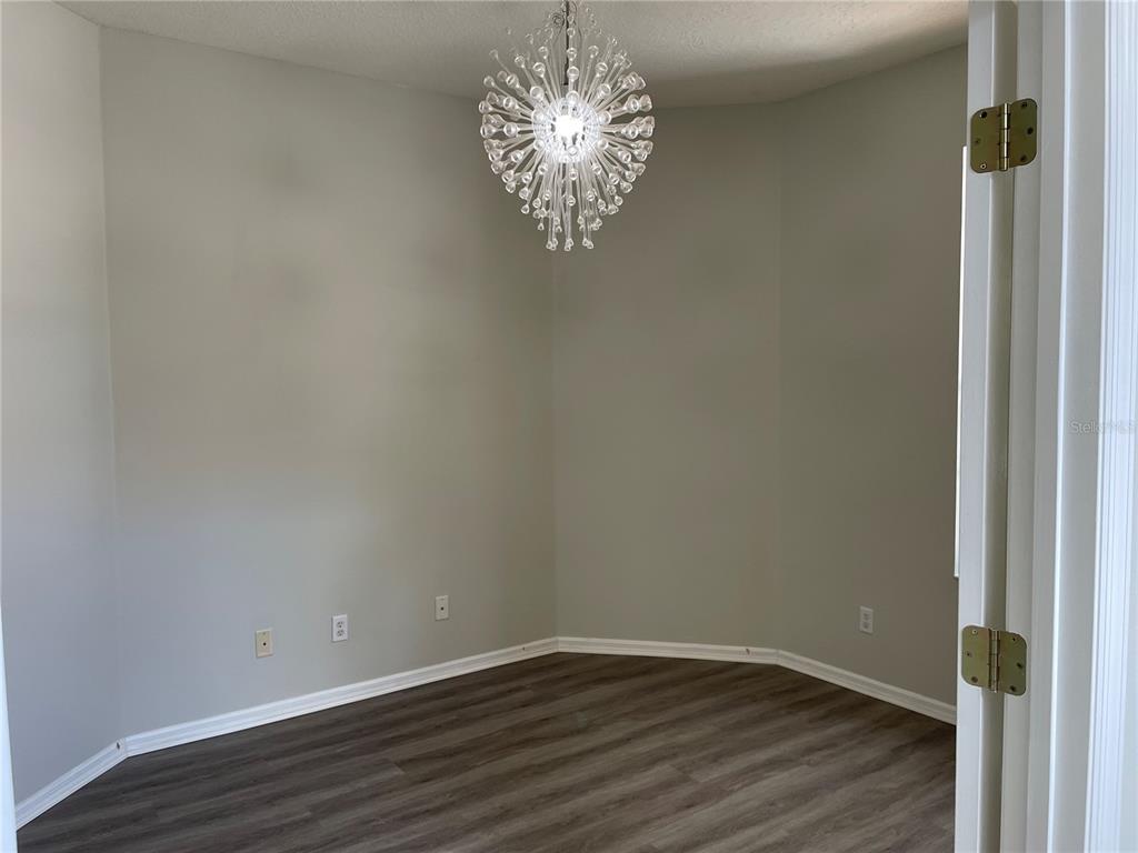 An empty room with gray walls, wood-look flooring, and a modern sputnik-style chandelier — 6119 PALOMINO CIRCLE, BRADENTON, FL