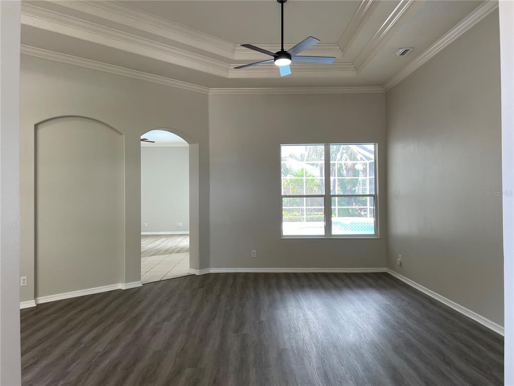 An empty room with gray wood-look flooring, a tray ceiling, and a view of a pool — 6119 PALOMINO CIRCLE, BRADENTON, FL