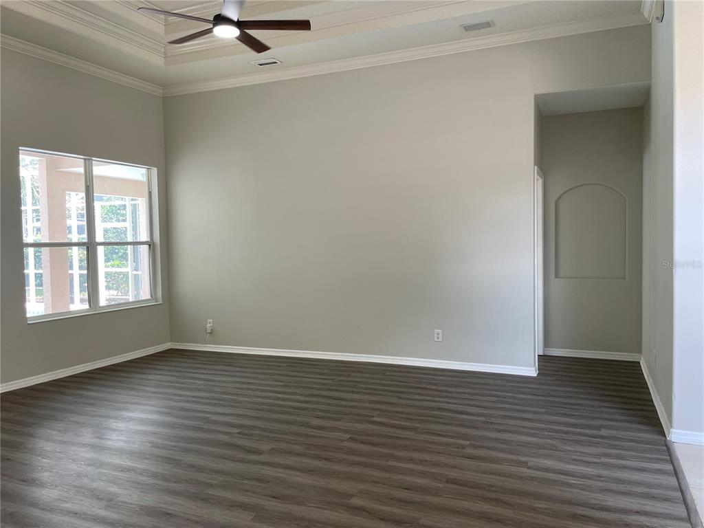 An empty living room features light gray walls, dark wood-look flooring, and a tray ceiling — 6119 PALOMINO CIRCLE, BRADENTON, FL