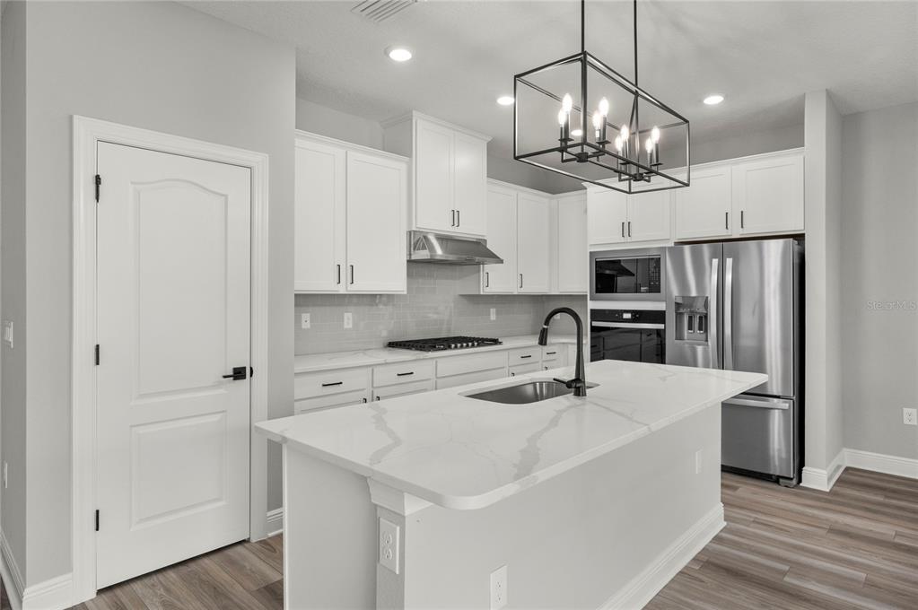 A modern kitchen features white cabinets, stainless steel appliances, a quartz island, and a pendant light — 7737 SOMERSWORTH DRIVE, KISSIMMEE, FL